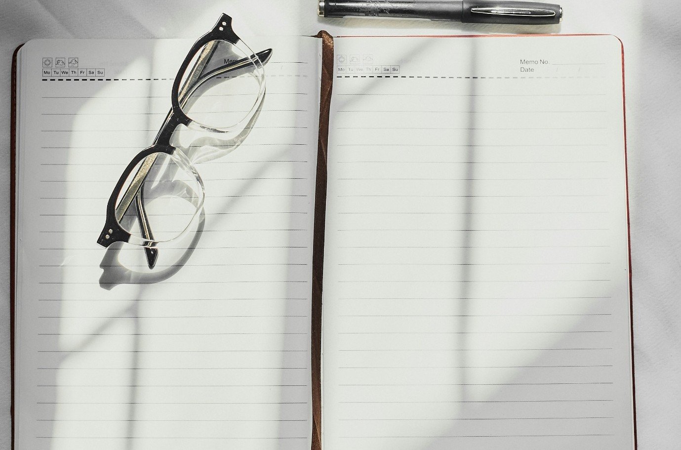 An open journal, glasses and a pen in soft window light